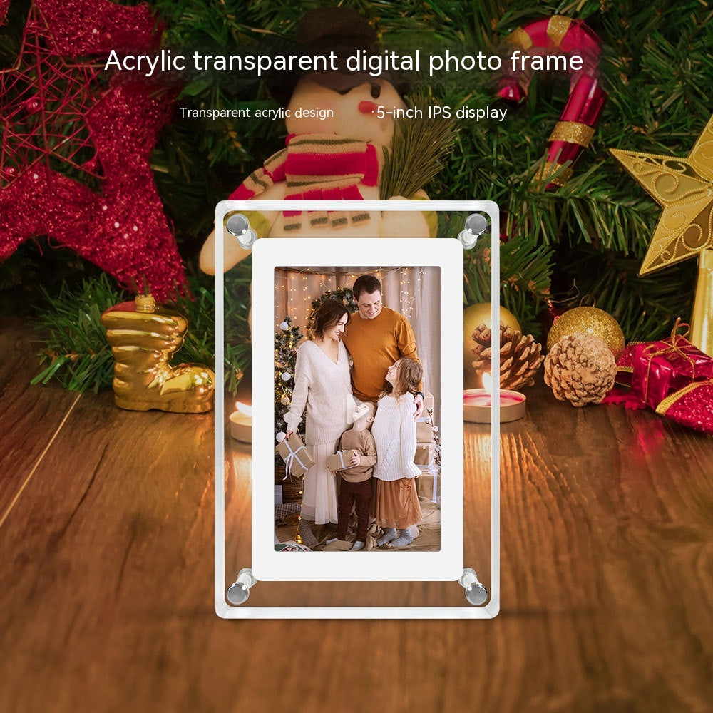 Transparent acrylic digital photo frame with a 5-inch IPS display on a wooden surface, surrounded by festive holiday decorations. The frame showcases a warm family photo of three individuals in a cozy, Christmas-themed setting. The overall scene creates a feeling of holiday warmth and family togetherness, highlighted by the frame's modern and sleek design.