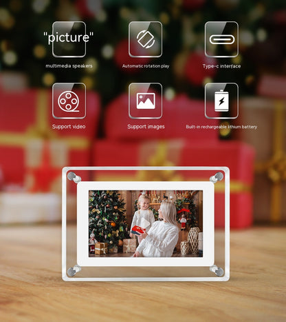 Transparent acrylic digital photo frame with a "picture" caption, featuring multimedia speakers, automatic rotation play, and a Type-C interface. The frame supports video and images, and has a built-in rechargeable lithium battery. It displays a festive photo of two people exchanging gifts by a Christmas tree, set against a backdrop of holiday decorations and wrapped presents.