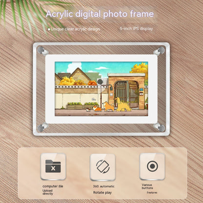 A digital photo frame with a unique clear acrylic design and an 8-inch IPS display, placed on a textured surface with palm leaves in the background. The frame displays a colorful, stylized image of a quaint street scene. Below the frame are icons indicating features such as direct computer file upload, 360-degree automatic rotation, and various button functions.
