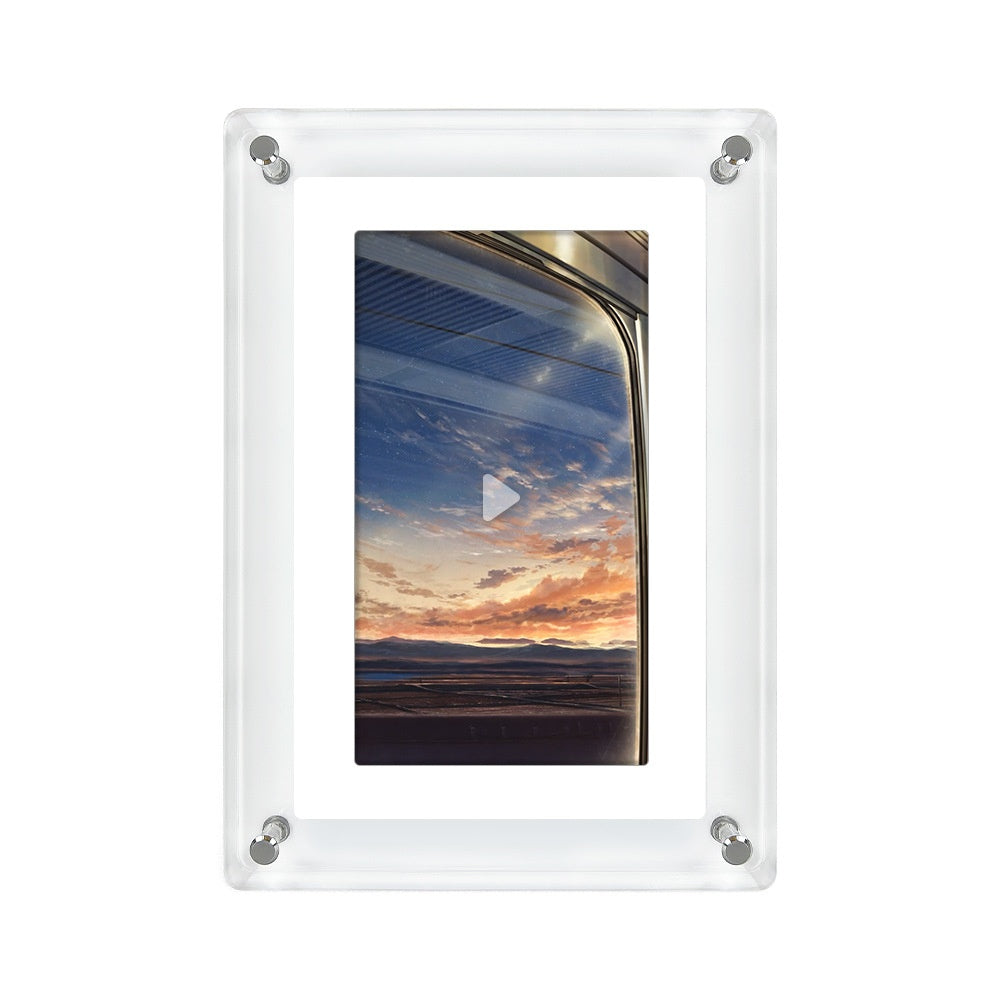 Transparent acrylic digital photo frame with a play button overlay indicating video functionality. The frame displays an image of a scenic sunset viewed through a vehicle window, captured against a vibrant sky with streaks of orange and blue. The sleek design of the frame is accentuated by four silver corner fastenings against a white background.